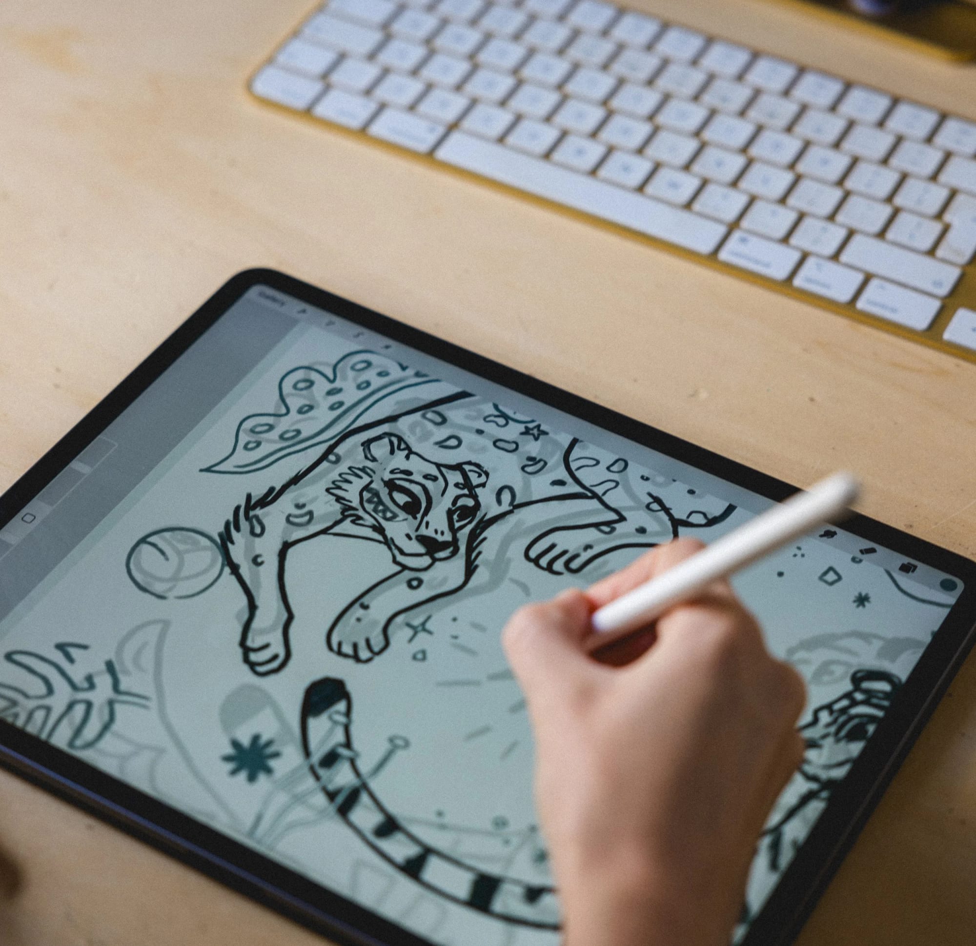 A person using a stylus to draw a lion on a digital tablet, with a keyboard in the background.